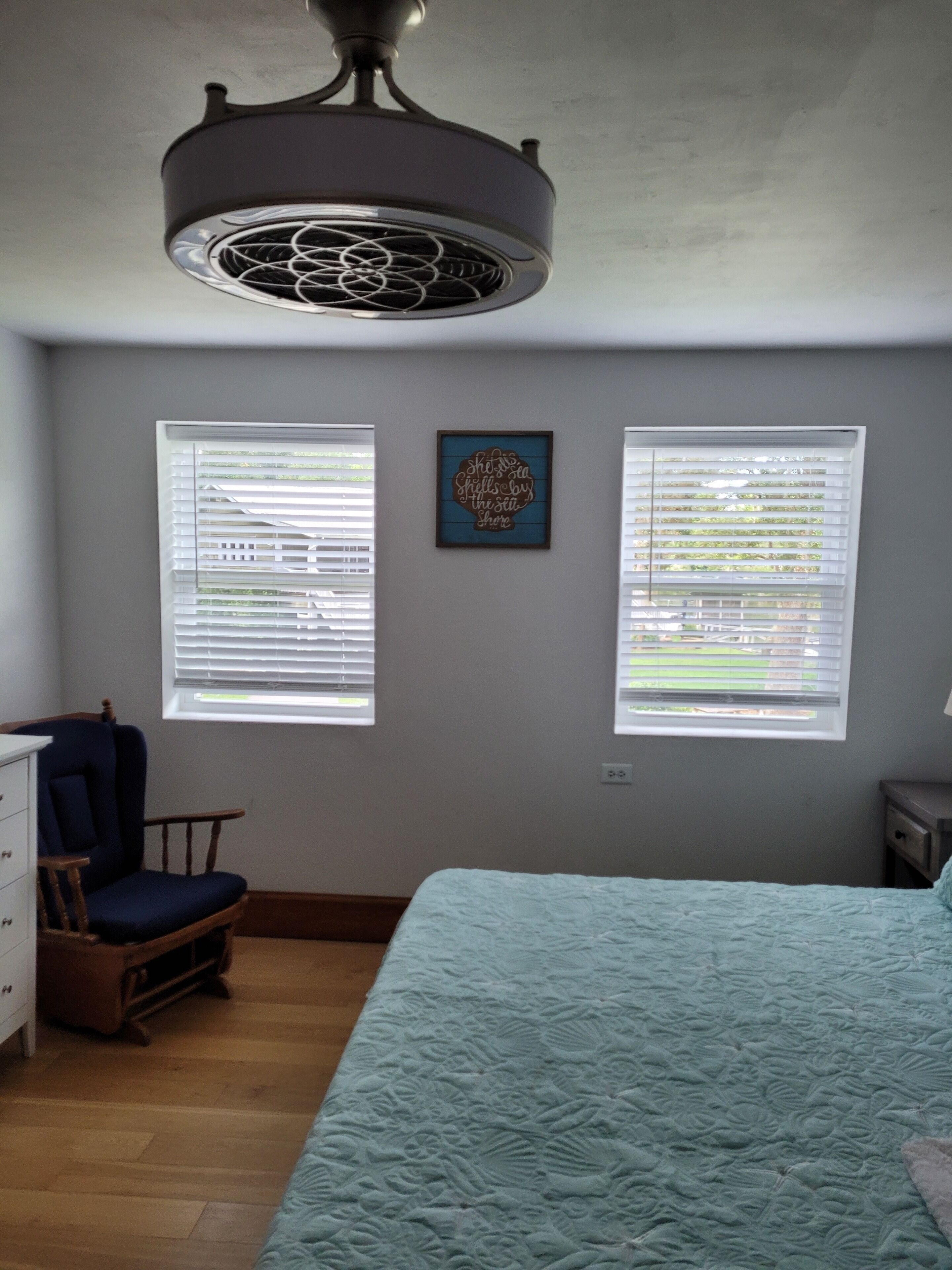 A bedroom with a bed, a chair, a dresser, and two windows with blinds.