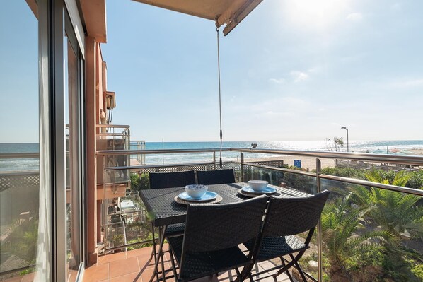 Un balcon avec une table et des chaises, donnant sur une plage et l’océan.