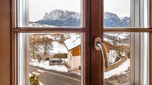 A view through a window with a wooden frame, snow-covered landscape, and a mountain in the background. - Holiday Apartment "Florerhof Lavendel" with Mountain View, Sauna, Wi-Fi & Garden (Völs am Schlern)