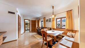 A modern interior with a wooden dining table, chairs, a sofa, and a view of the outdoors. - Holiday Apartment "Florerhof Lavendel" with Mountain View, Sauna, Wi-Fi & Garden (Völs am Schlern)