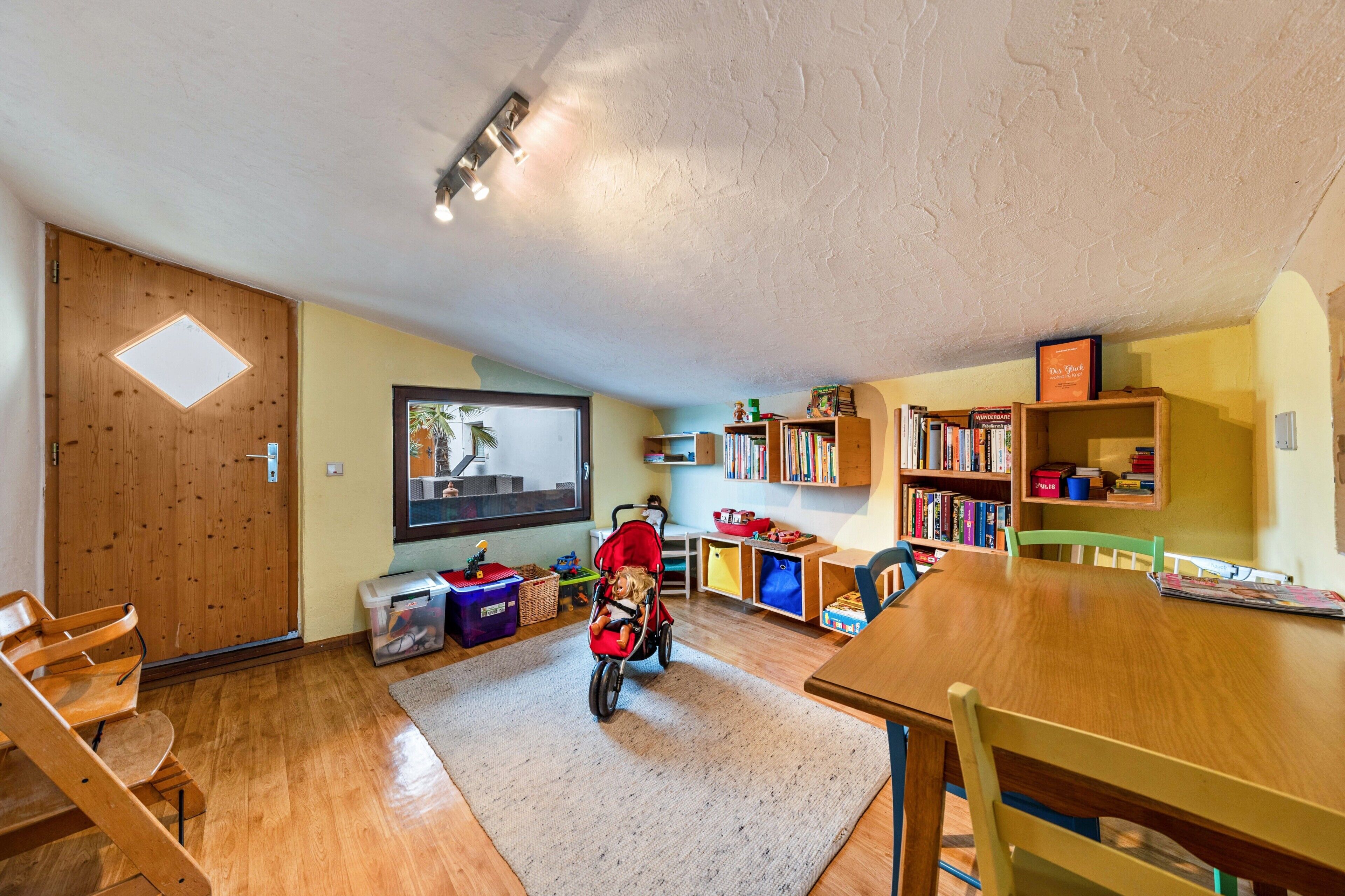 A room with a wooden floor, a TV, a bookshelf, a table, and a stroller.