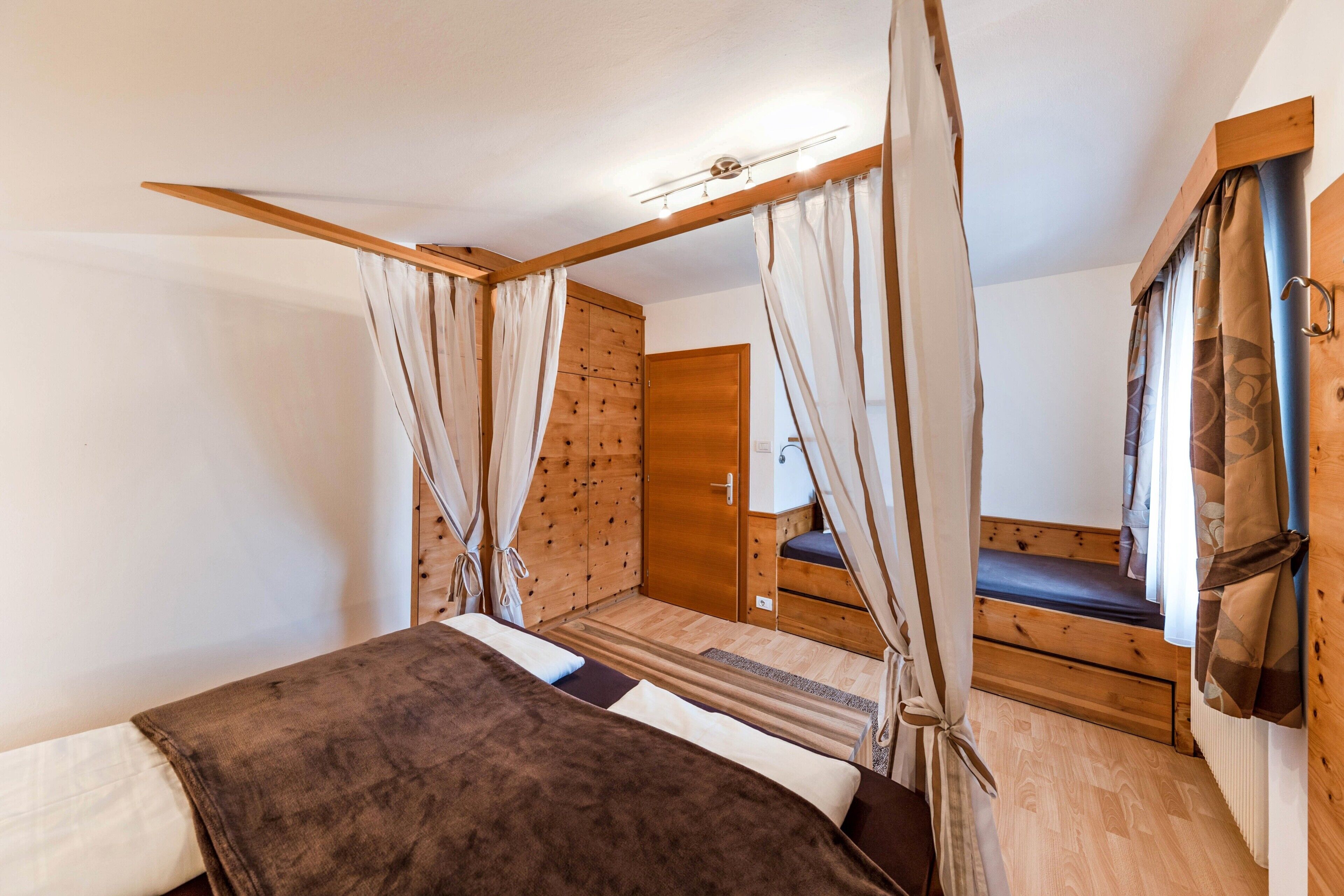 A bedroom with a bed, wooden wardrobe, and a small seating area.