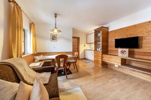 A living room with a sofa, dining table, chairs, a TV, wooden cabinets, and a wooden wall.