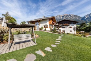 Una casa grande con terraza de madera, camino de piedra y montañas al fondo.
