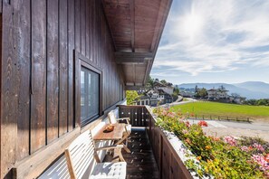 A wooden balcony with a table and chairs, overlooking a green landscape and houses. - Holiday Apartment "Florerhof Flieder" with Mountain View, Sauna, Wi-Fi & Garden (Völs am Schlern)