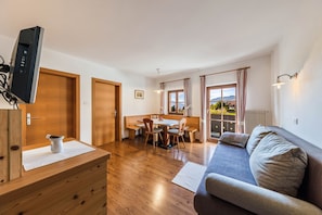 A modern living room with a wooden dining table, a sofa, and a television mounted on a wooden cabinet.