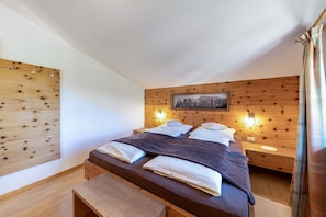 A bedroom with a wooden headboard, a bed with white and dark bedding, a bedside table with a lamp, and a wooden bench.