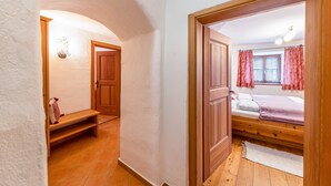 Ein Schlafzimmer mit einem hölzernen Bett, einem Fenster mit Vorhängen, einer Bank und einer Tür zu einem anderen Raum.