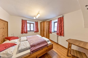 A bedroom with a wooden bed, red curtains, a wooden table, and a ceiling light fixture.
