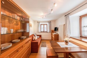 A cozy living room with a sofa, a wooden dining table, and a glass cabinet with dishes.