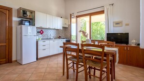 Una cocina moderna con armarios blancos, horno empotrado y una zona de comedor con sillas y mesa de madera.