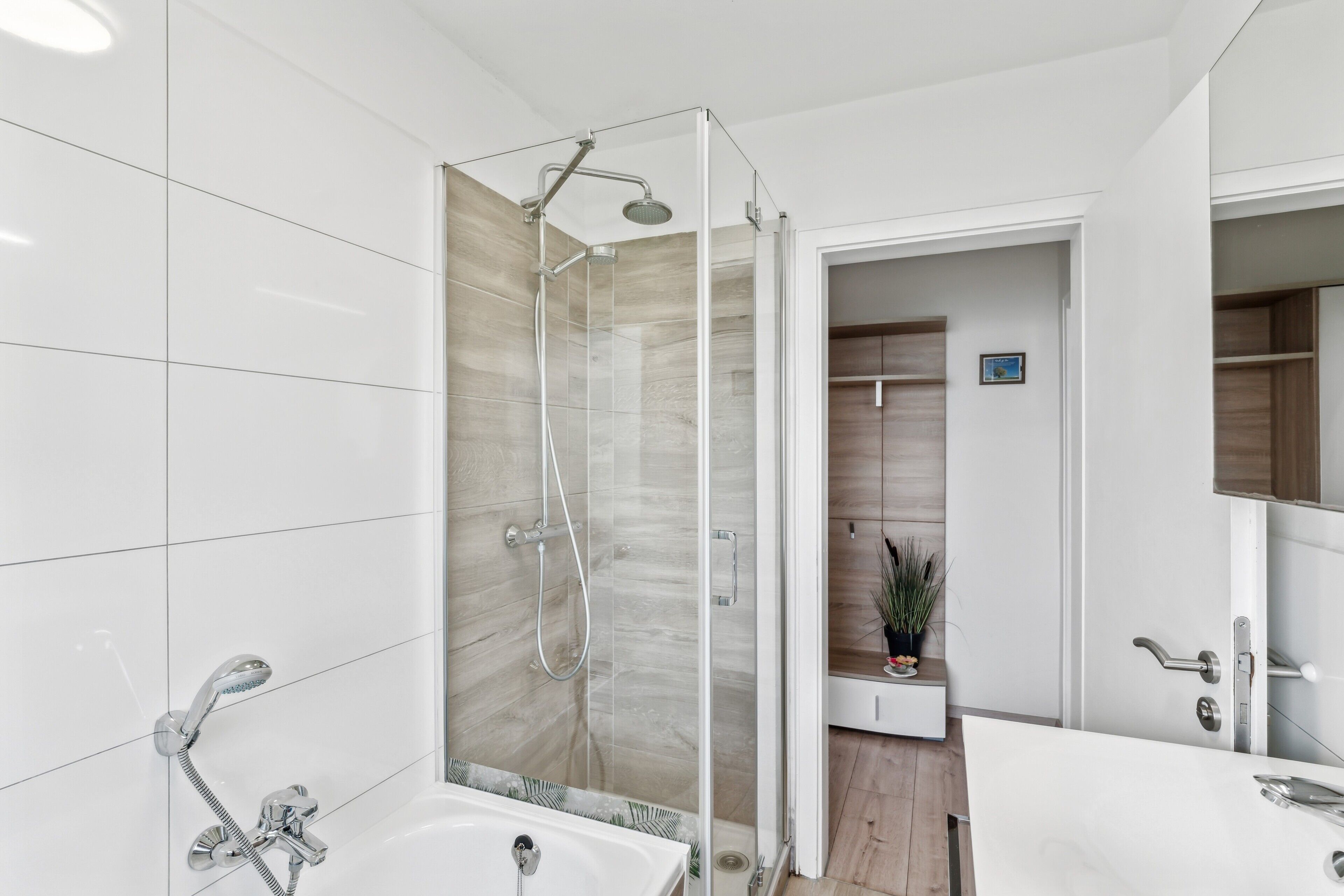 Ein modernes Badezimmer mit einer gläsernen Dusche, einer weißen Badewanne und einem Holzwaschtisch.