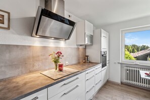 Une cuisine moderne dotée d’un four encastré, d’une hotte en acier inoxydable et d’une fenêtre donnant sur un paysage verdoyant.