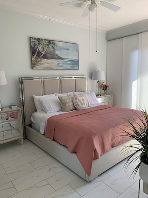 Une chambre à coucher comprenant un lit, des tables de chevet, une commode, un ventilateur de plafond, un tableau et une plante en pot.
