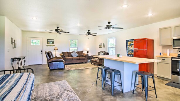 Amplia sala de estar con sofá, mesa de centro y cocina con refrigerador rojo y taburetes de bar.