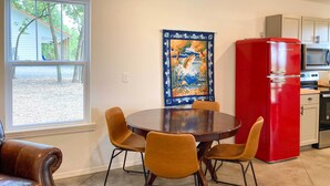 Un comedor con una mesa redonda y cuatro sillas, un refrigerador rojo y una cocina con microondas.