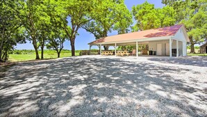 Un pabellón cubierto con mesas de picnic, rodeado de árboles y suelo de grava.