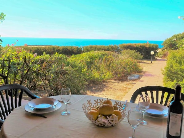A table set for dining with a view of the ocean, a bottle of wine, and a basket of bread rolls. - Vacation home Cisto by Interhome (Costa Paradiso)