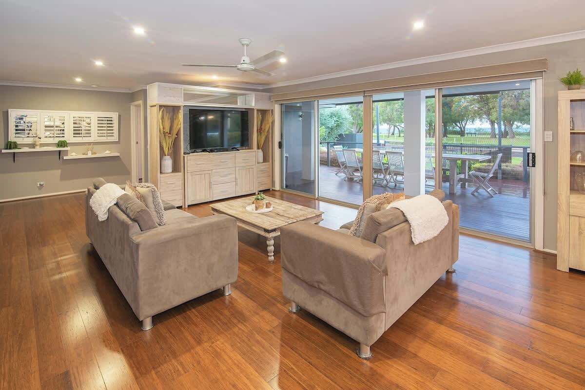 A spacious living area with a sofa set, a flat-screen TV, and a sliding glass door leading to an outdoor patio.