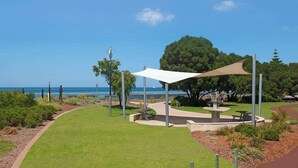 Een park met een picknickplaats, een witte luifel en uitzicht op de oceaan.