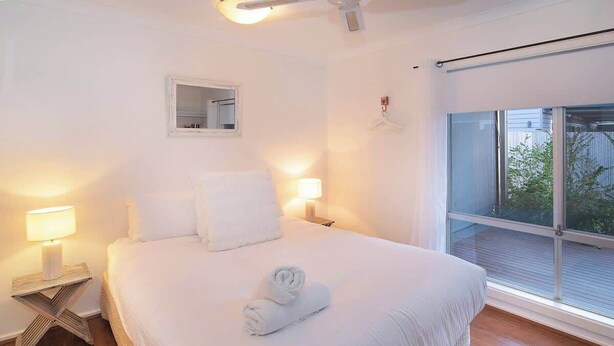 Een slaapkamer met een groot bed, twee nachtkastjes met lampen, een spiegel en een raam met uitzicht.