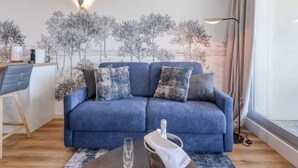 Ett modernt vardagsrum med en blå soffa, ett soffbord och en dekorativ väggmålning.