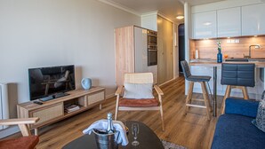 Ett modernt vardagsrum med tv, en matplats med bardisk och ett kök med vita skåp.