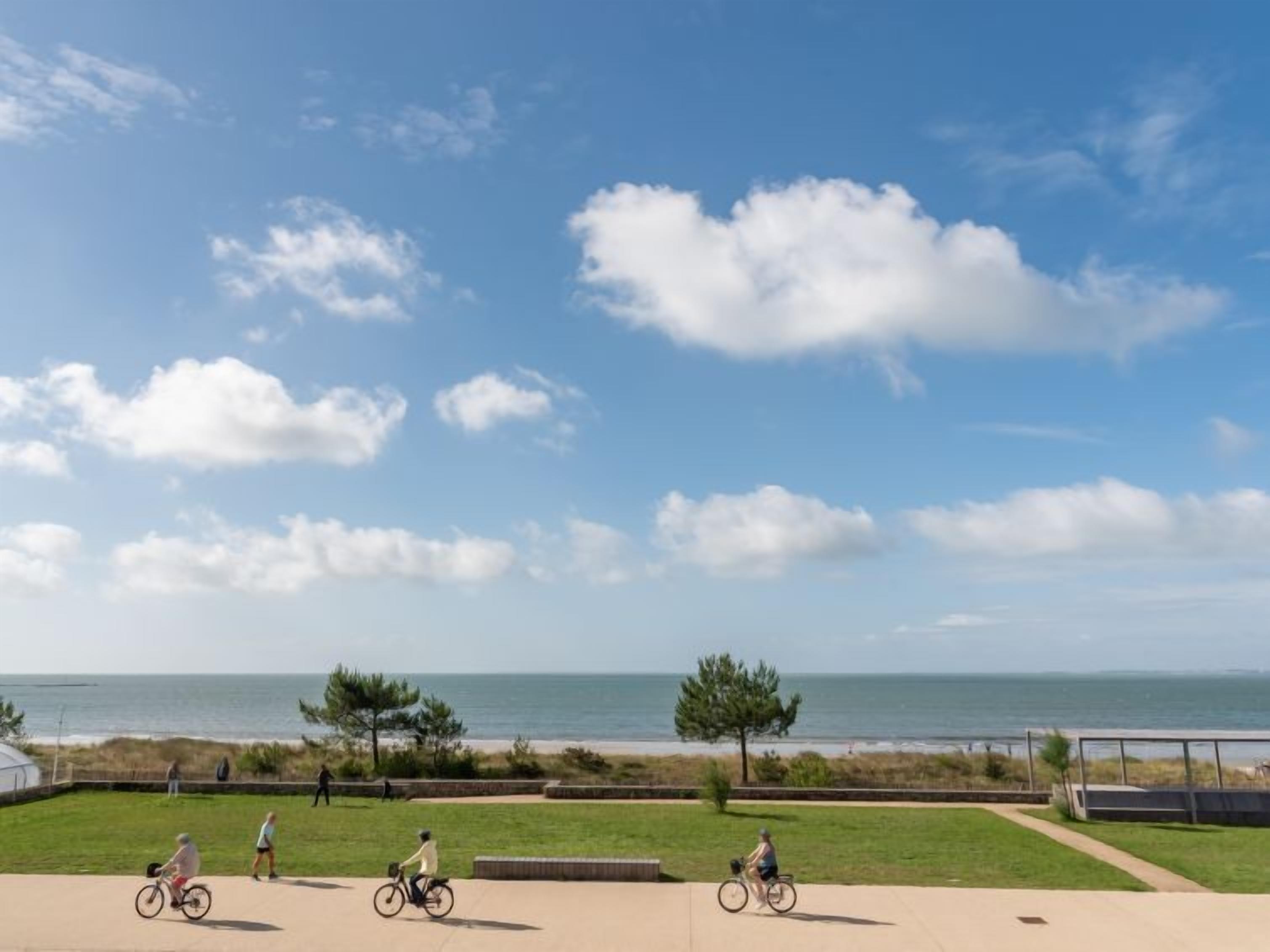 A coastal park with a paved walkway, grassy areas, and a view of the ocean.