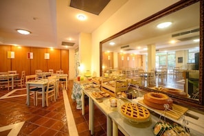Ein Hotel-Speisesaal mit mehreren Tischen, einem Buffet mit verschiedenen Speisen und einem großen Spiegel, der den Raum widerspiegelt.