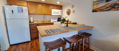 A modern kitchen with wooden cabinets, a white refrigerator, a built-in island with stools, and a painting on the wall.