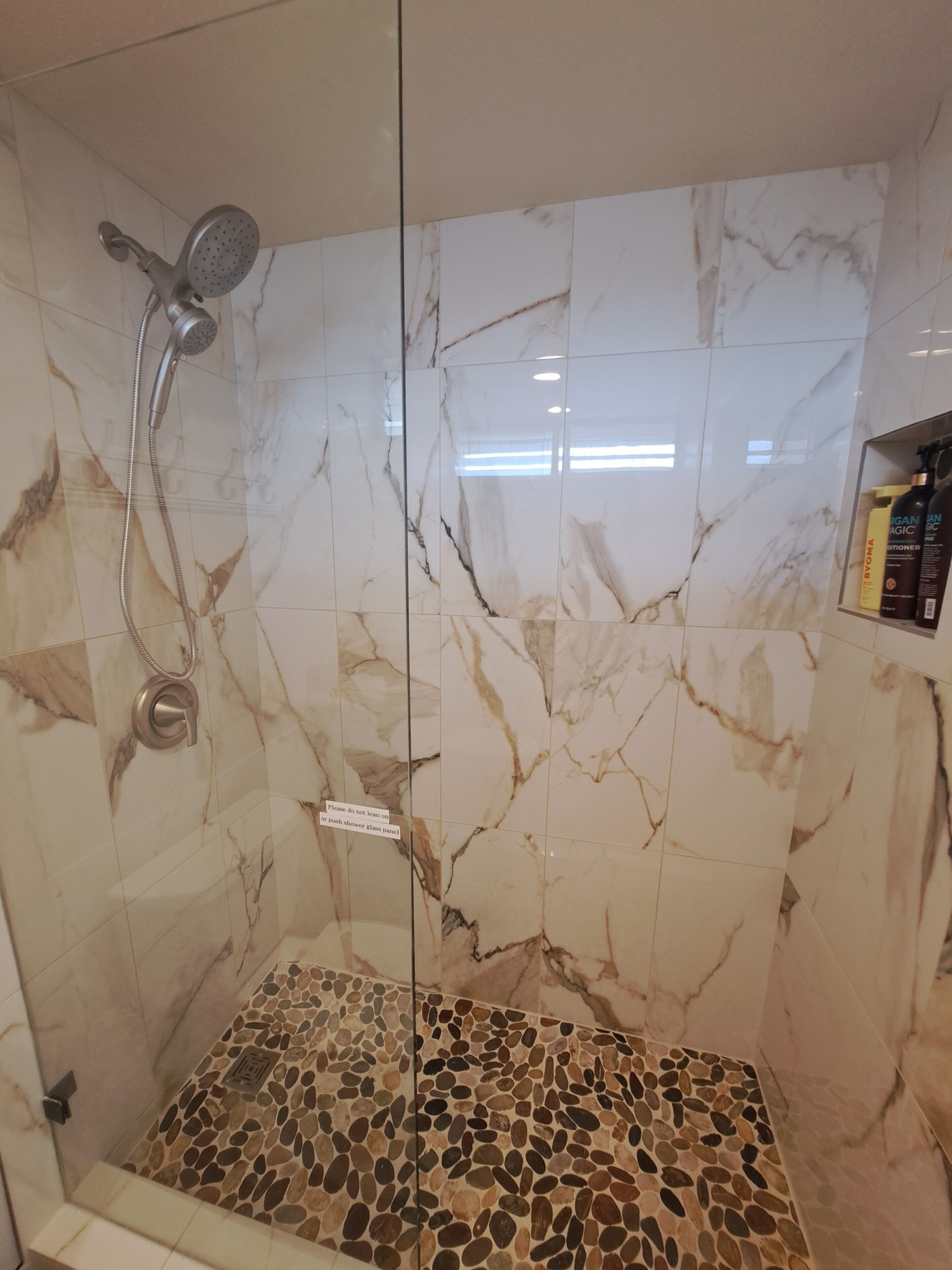 A shower with a glass door, marble tiles, and a mosaic floor.
