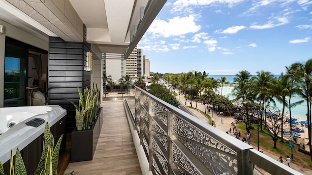 Un balcón con vista a la playa, palmeras y un paisaje urbano.