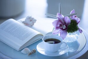 Un llibre obert, una tassa de cafè, un arranjament floral i petxines sobre un plat.