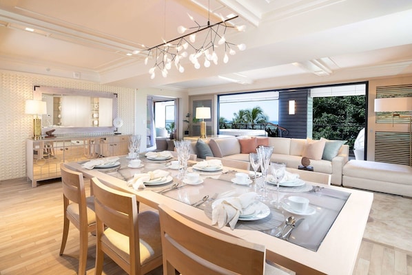 Un comedor amplio con una mesa larga dispuesta para una comida, una cocina moderna al fondo y vistas al exterior.