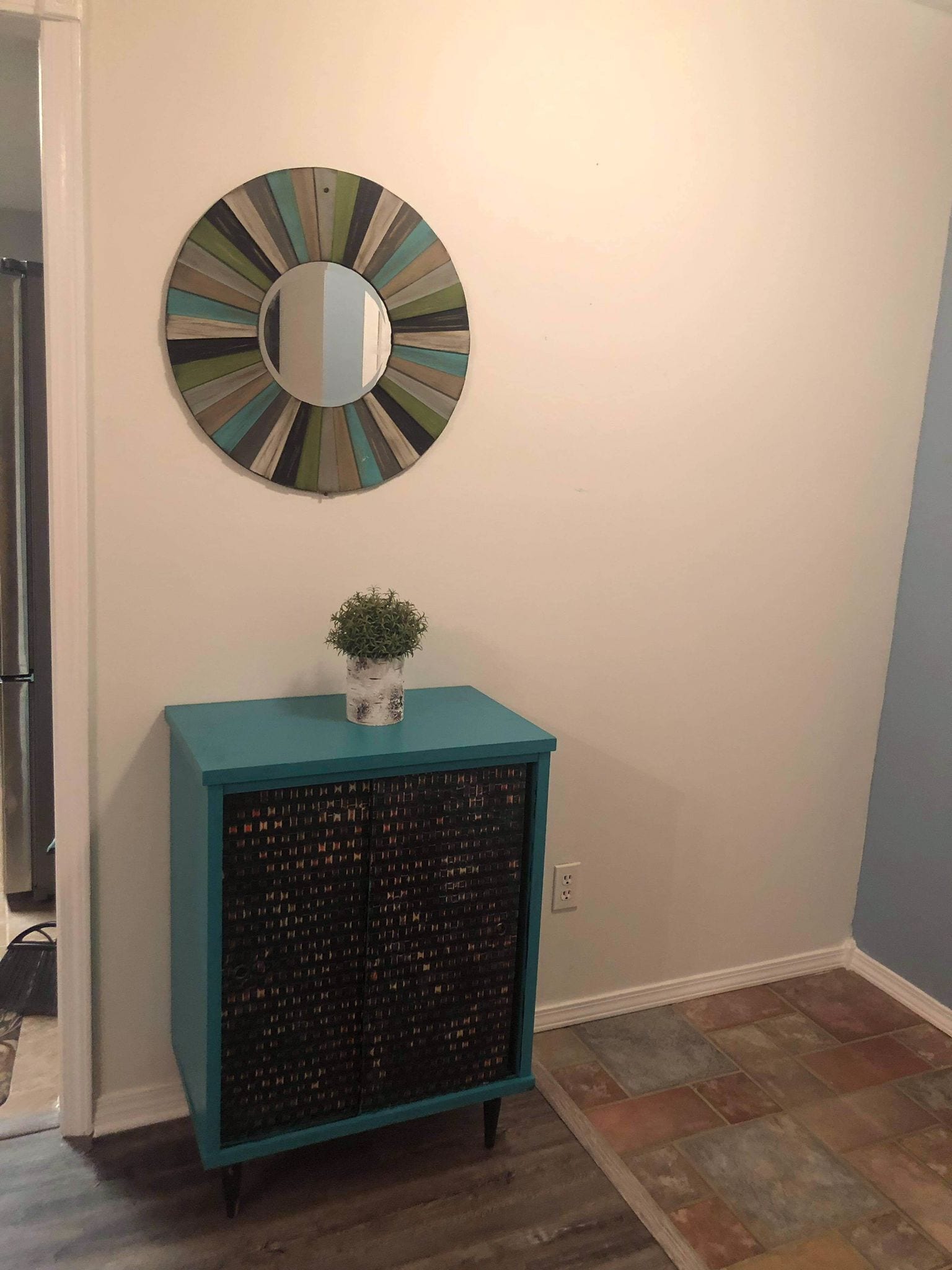 A teal cabinet with a mirrored top and a small potted plant on it.