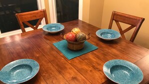 Een houten eettafel met vier blauwe borden, een decoratieve kom met fruit in het midden, en twee houten stoelen.