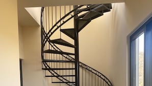 Een spiltrap met een zwarte metalen balustrade, plantenpotten en een uitzicht door een glazen deur naar buiten.
