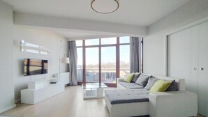 Un salon moderne avec un canapé blanc, un téléviseur à écran plat et une grande fenêtre donnant sur la ville.