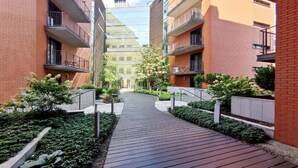 Un immeuble d’appartements moderne doté d’une cour intérieure, avec un chemin en bois et de la verdure.