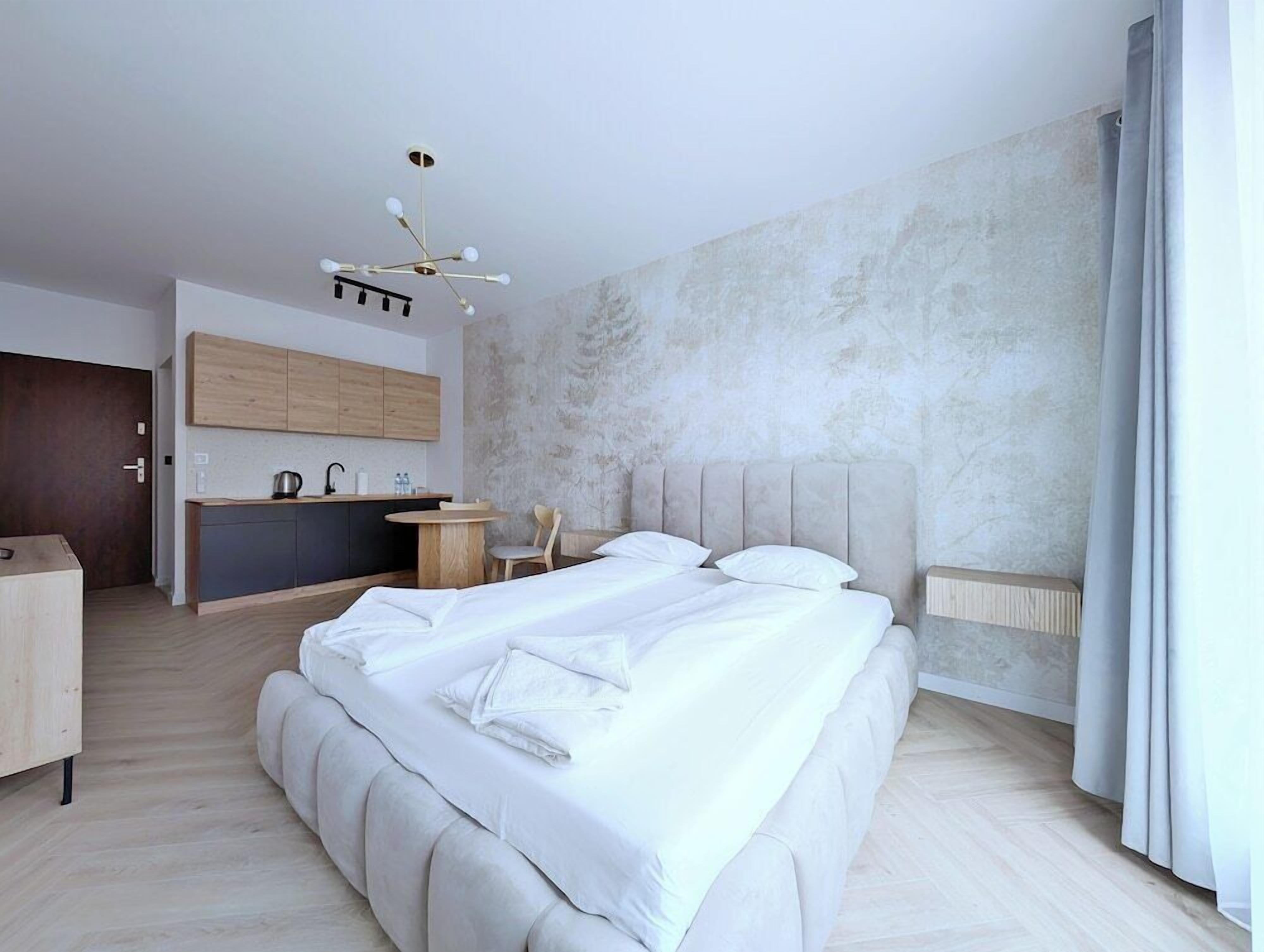A modern bedroom with a large bed, a small kitchenette, and a dining area.
