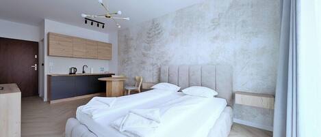 A modern bedroom with a large bed, a small kitchenette, and a dining area.