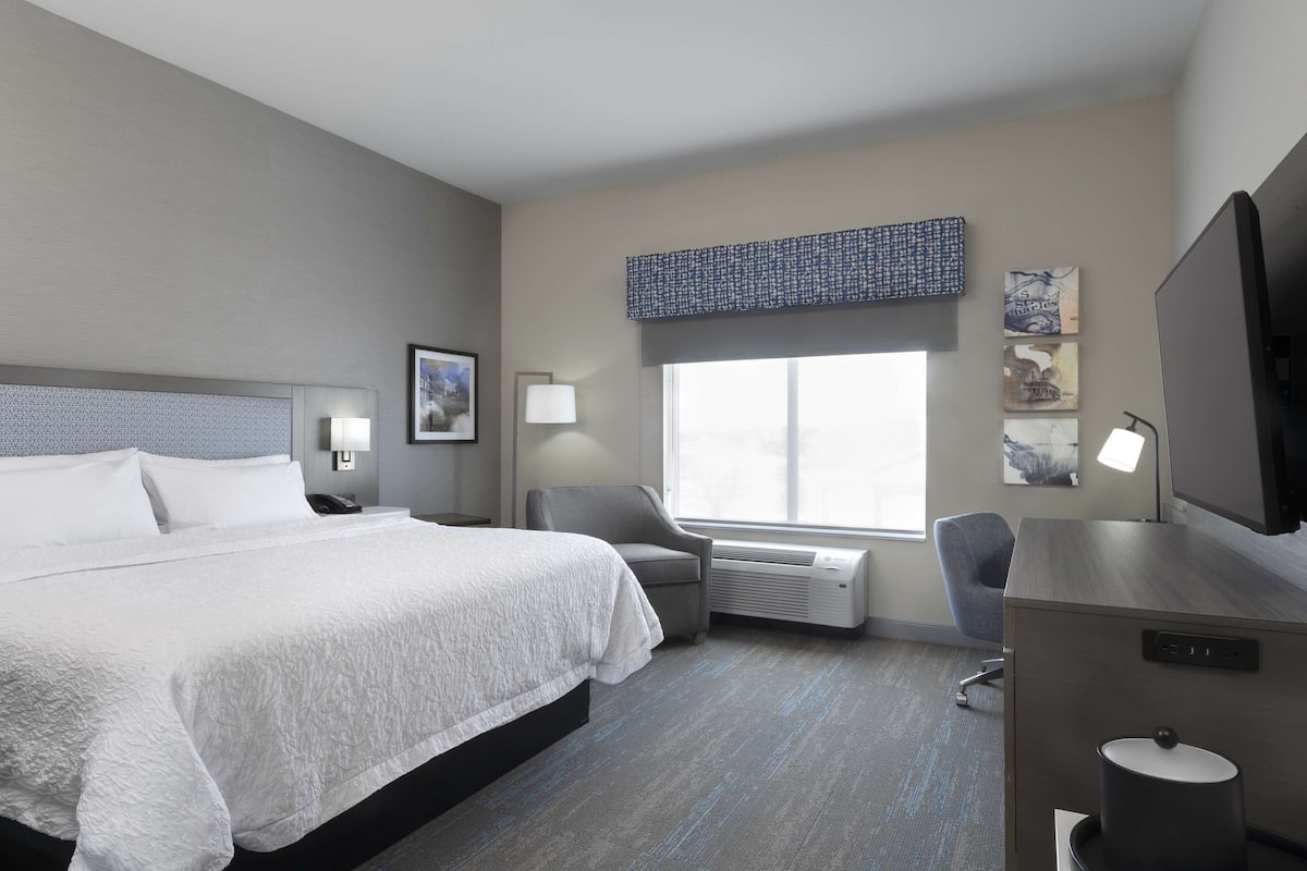 A hotel room with a large bed, a desk, a chair, and a window with a view.