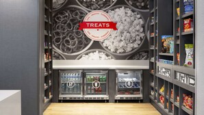 Un espace dédié aux collations et aux boissons, avec un panneau indiquant « Friandises », des distributeurs de boissons réfrigérés et des étagères remplies de collations et de boissons.