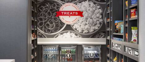 A snack and drink area with a 'Treats' sign, refrigerated drink dispensers, and shelves stocked with snacks and beverages.
