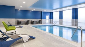 Une piscine intérieure aux murs bleus, avec un sol carrelé et des chaises longues.