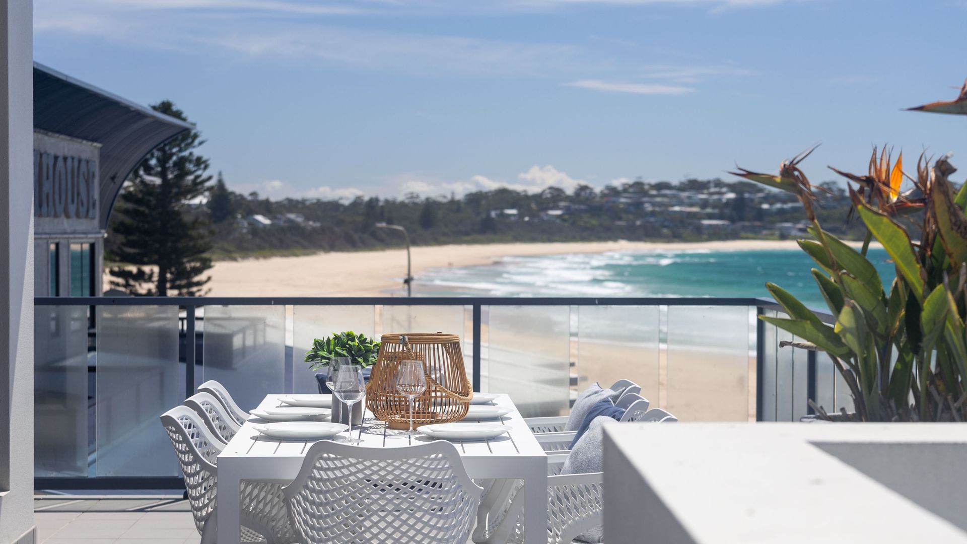 Un balcón con una mesa dispuesta para comer, con vista a una playa y el océano.