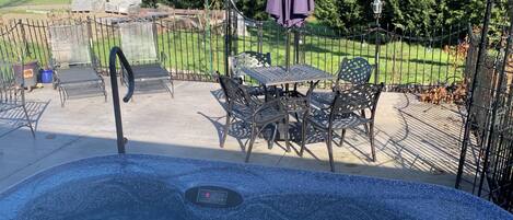 A hot tub with a control panel, surrounded by patio furniture and a purple umbrella.