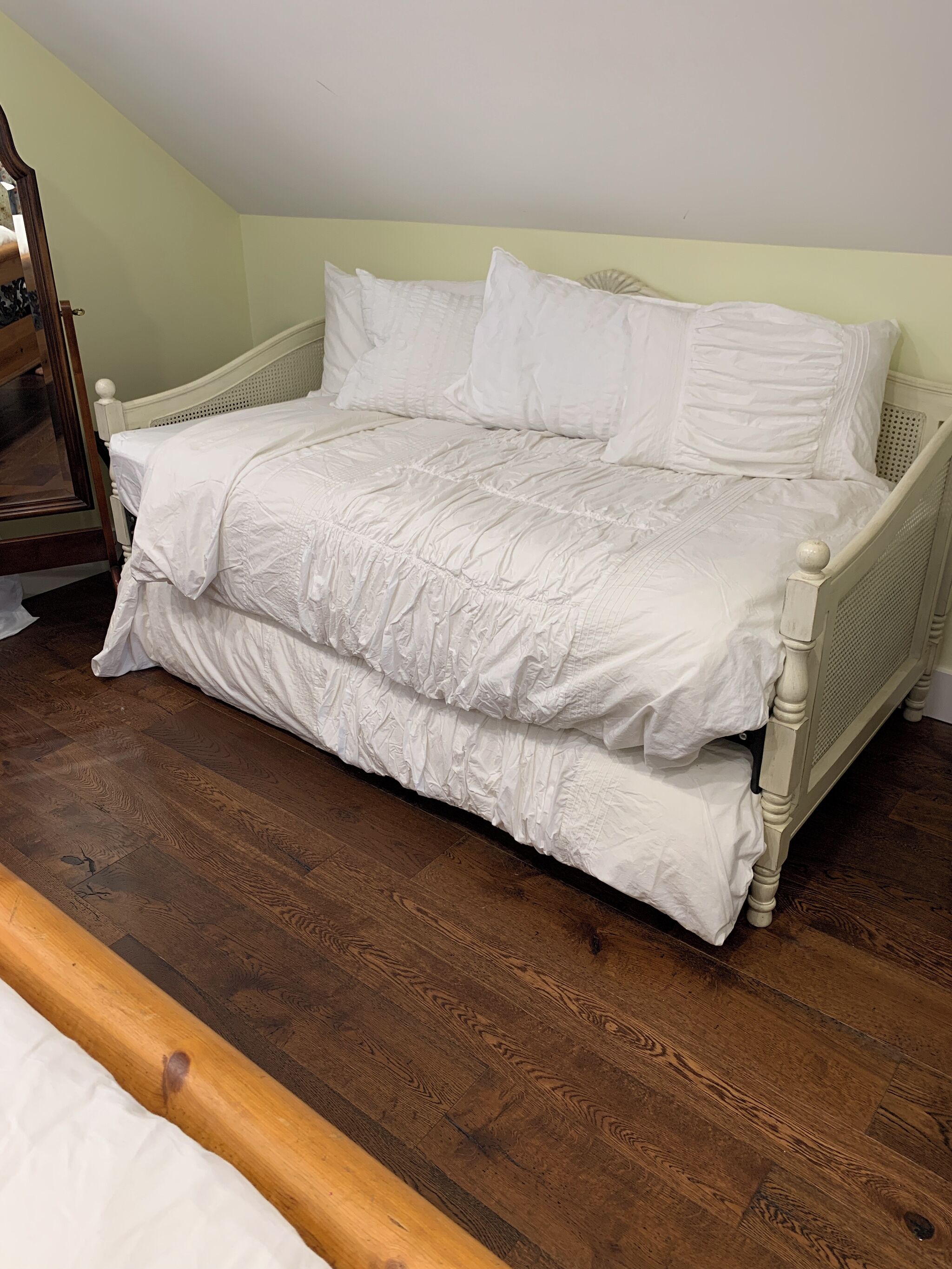 A single bed with a wooden frame and white bedding in a room with wooden flooring and light green walls.