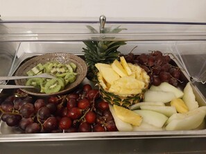 Un buffet proposant des kiwis, des ananas, des raisins et des pommes, le tout présenté en tranches.