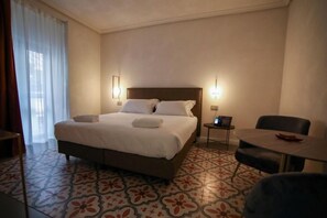 Quarto de hotel com uma cama grande, uma mesa pequena, uma cadeira e uma escrivaninha com um computador.